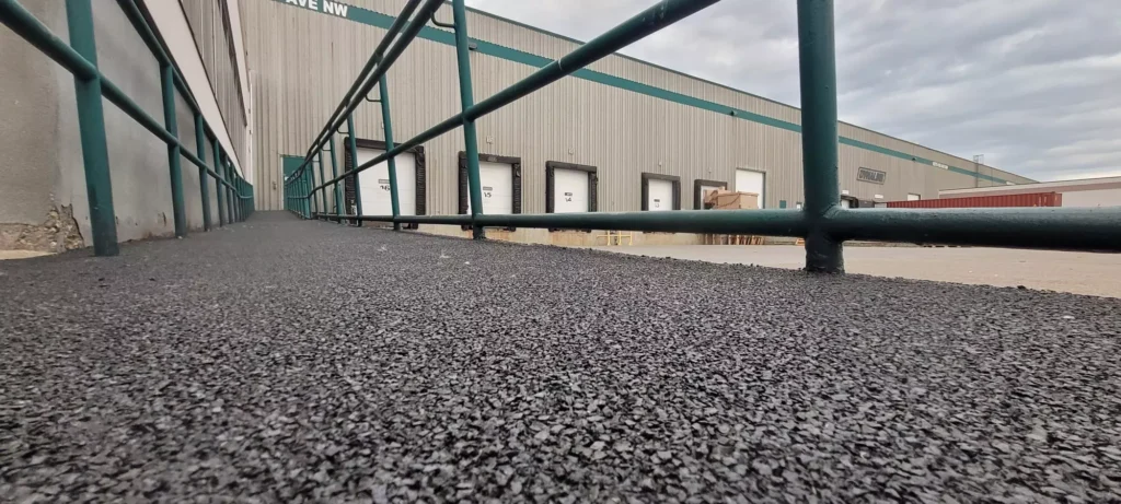 Close-up view of textured rubber paving surface along an industrial ramp near a warehouse, demonstrating durable paving used in asphalt repair and concrete construction projects