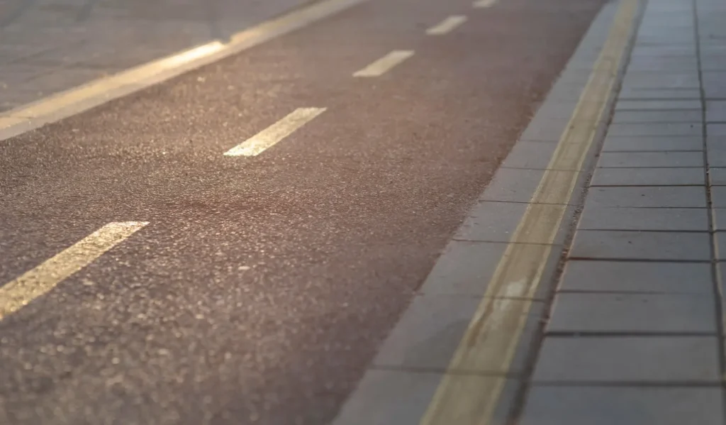 Smooth asphalt road surface with painted lines next to sidewalk, showing results of asphalt repair and ongoing commercial property maintenance including concrete repair work