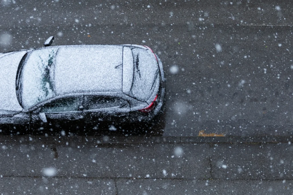 Car parked on the roadside during snowfall, illustrating the need for parking lot snow removal and proper Parking Lot Maintenance in winter conditions. 
