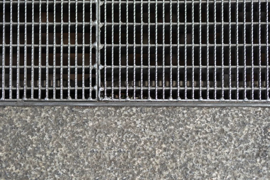 Metal grate over drainage opening prepared for catch basin repair in urban pavement