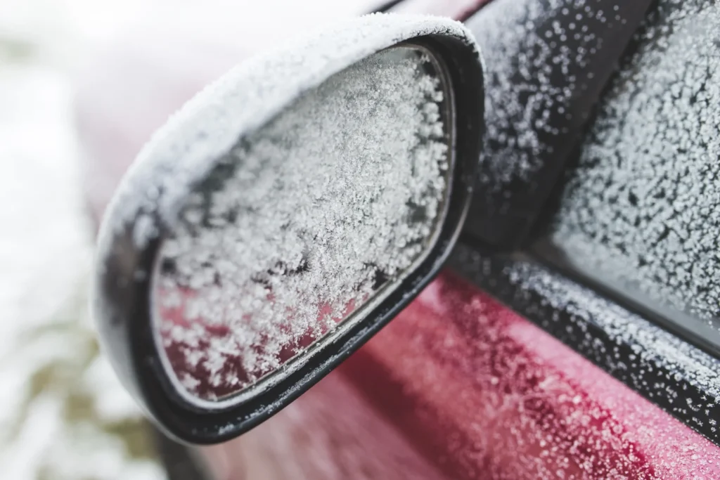 Side mirror covered with frost and snow - winter safety and snow removal challenges for vehicles