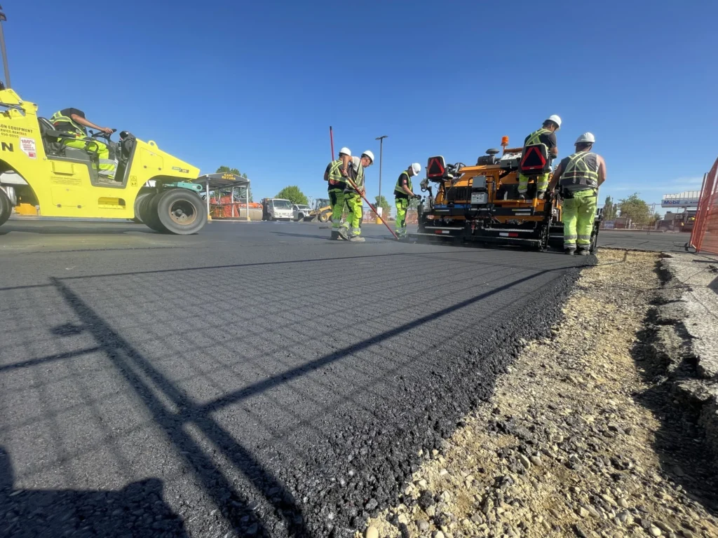 A team of construction workers operates paving equipment while laying asphalt roads on a clear day.