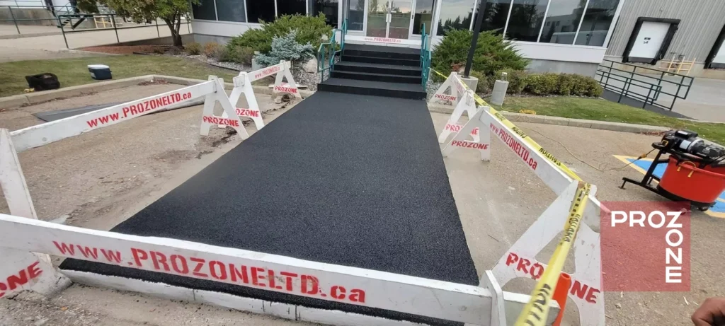 Workers smooth a new black asphalt surface leading to a building entrance as they carry out what is paving.
