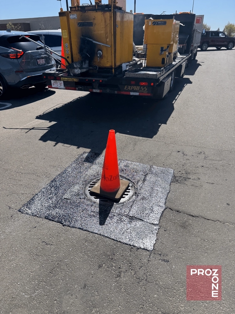 Orange cone placed on a patched section of asphalt around a drain showing how to repair pothole.
